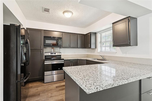 601 Jw Davis Dr, Hammond, LA 70403 - kitchen with black appliances, a peninsula, wood finished floors, a textured ceiling, and light stone counters