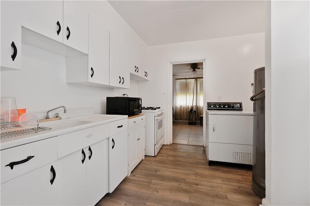 2727 Carondelet St, New Orleans, LA 70130 - kitchen with washer / clothes dryer, black microwave, white cabinetry, light wood finished floors, and gas range gas stove