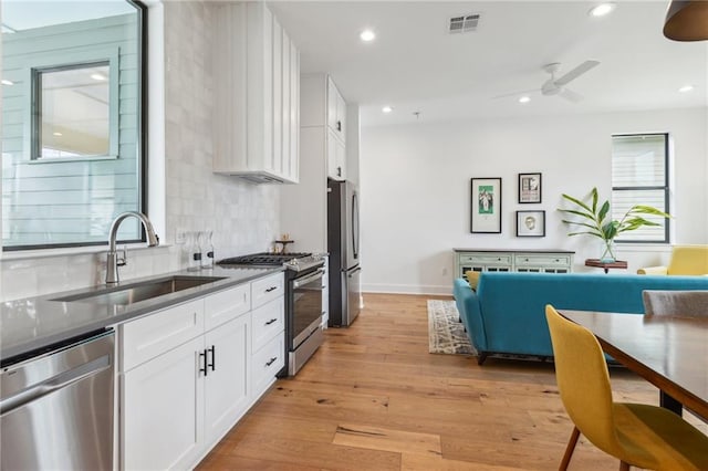 810 N Roman St, New Orleans, LA 70116 - kitchen with appliances with stainless steel finishes, light wood finished floors, white cabinets, backsplash, and ceiling fan