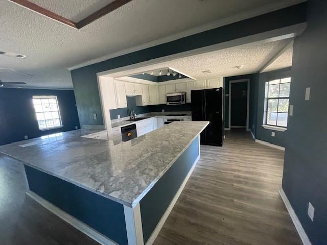 14151 W Hoffman Rd, Hammond, LA 70403 - kitchen featuring stainless steel microwave, a textured ceiling, white cabinets, freestanding refrigerator, and a peninsula