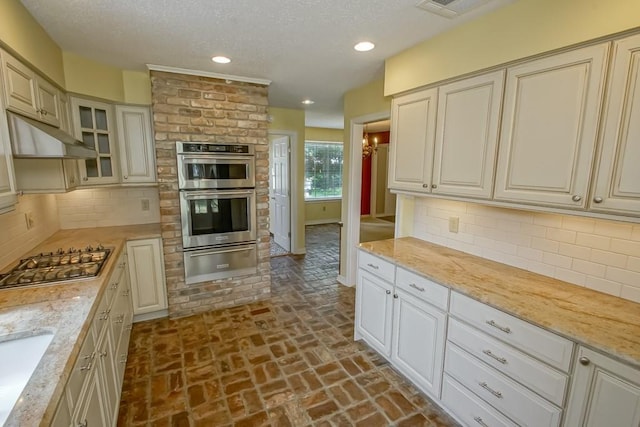 8808 Chretien Point Pl, River Ridge, LA 70123 - kitchen featuring a warming drawer, appliances with stainless steel finishes, brick flooring, under cabinet range hood, and a textured ceiling