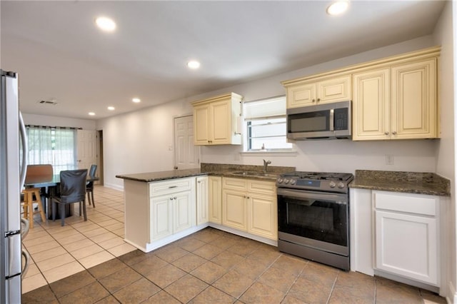 2808 Transcontinental Dr, Metairie, LA 70006 - kitchen featuring appliances with stainless steel finishes, cream cabinetry, a peninsula, recessed lighting, and dark stone countertops