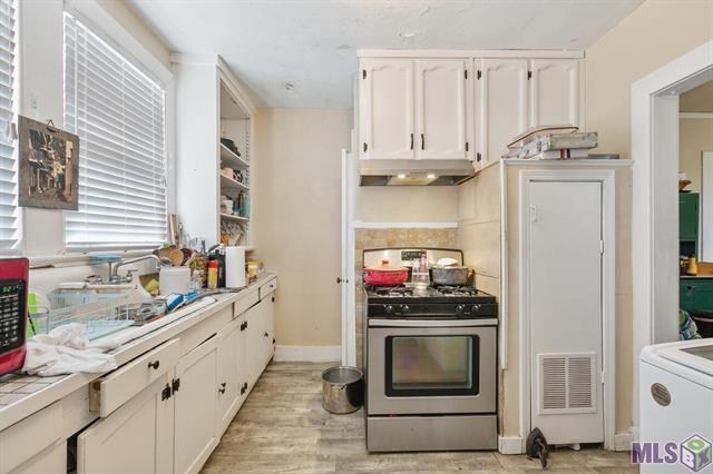 21416 N 12th St, Baton Rouge, LA 70802 - kitchen with stainless steel gas range, under cabinet range hood, white cabinets, tile countertops, and washer / dryer