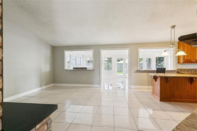 4000 Kawanee Ave, Metairie, LA 70002 - kitchen with healthy amount of natural light, a textured ceiling, light tile patterned floors, a breakfast bar area, and brown cabinetry