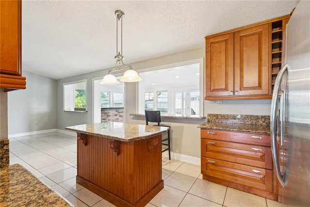 4000 Kawanee Ave, Metairie, LA 70002 - kitchen featuring stainless steel refrigerator, brown cabinetry, stone countertops, a kitchen bar, and a center island