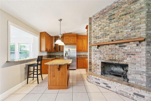 4000 Kawanee Ave, Metairie, LA 70002 - kitchen featuring stainless steel refrigerator with ice dispenser, brown cabinetry, light tile patterned flooring, a textured ceiling, and a center island