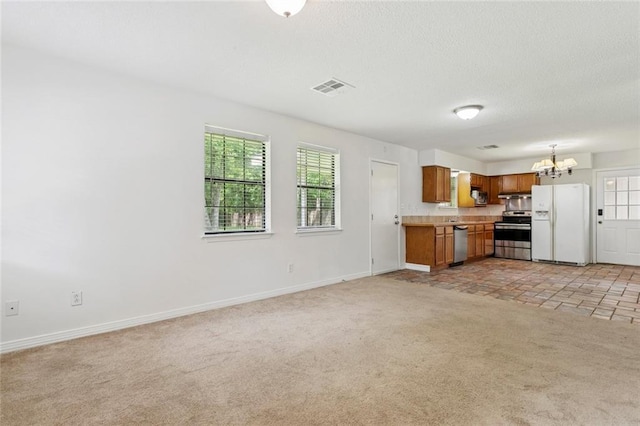 205 Timber Ridge Dr, Slidell, LA 70460 - kitchen with appliances with stainless steel finishes, brown cabinets, a chandelier, light colored carpet, and light countertops