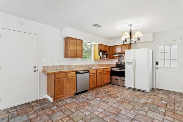 205 Timber Ridge Dr, Slidell, LA 70460 - kitchen with stainless steel appliances, a chandelier, light countertops, a textured ceiling, and brown cabinetry