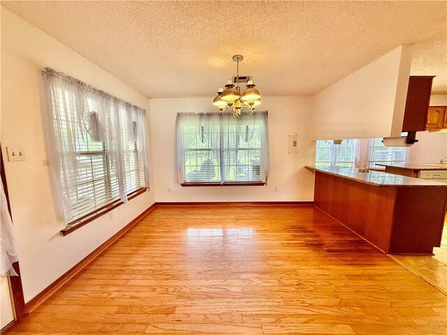 7282 Barataria Blvd, Marrero, LA 70072 - unfurnished dining area featuring healthy amount of natural light, a chandelier, light wood finished floors, and a textured ceiling