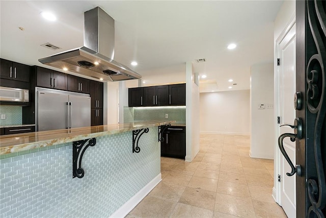 700 Crystal St, New Orleans, LA 70124 - kitchen with built in fridge, island exhaust hood, white microwave, decorative backsplash, and a breakfast bar