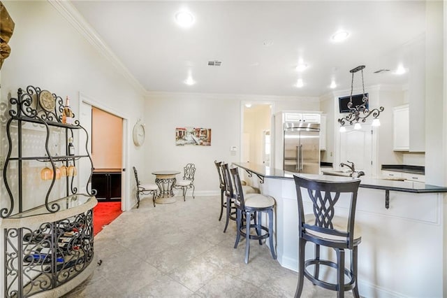 601 Ferriday Ct, Harahan, LA 70123 - kitchen with built in refrigerator, dark countertops, ornamental molding, a breakfast bar area, and white cabinets
