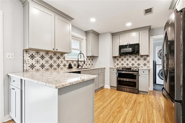 7032 Glenn St, Metairie, LA 70003 - kitchen featuring stainless steel appliances, estacked washer and dryer, gray cabinets, a peninsula, and light wood-style floors
