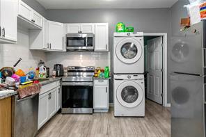 272 W Harrison St, Baton Rouge, LA 70802 - kitchen with stainless steel appliances, stacked washing machine and dryer, light wood finished floors, and white cabinets