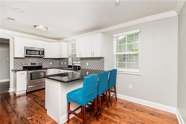 4108 Rayne Dr, New Orleans, LA 70122 - kitchen with stainless steel appliances, dark countertops, ornamental molding, white cabinets, and a kitchen bar