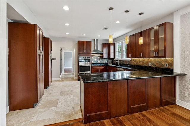 4752 Demontluzin St, New Orleans, LA 70122 - kitchen featuring wall chimney range hood, a peninsula, appliances with stainless steel finishes, decorative backsplash, and glass insert cabinets