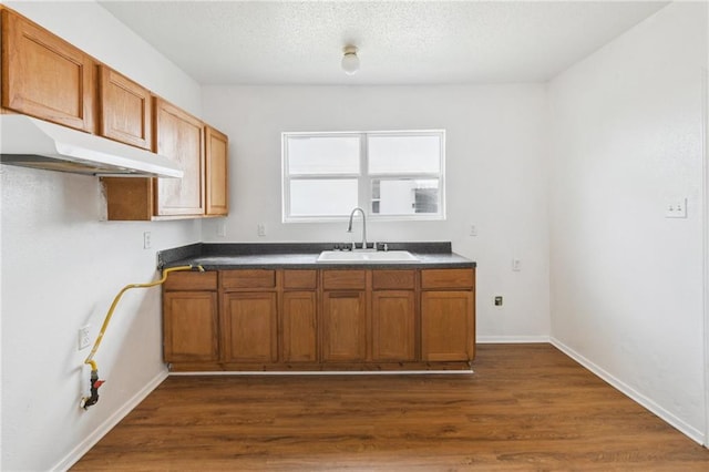 4601 Reynes St, New Orleans, LA 70126 - kitchen with under cabinet range hood, brown cabinetry, dark wood finished floors, and dark countertops