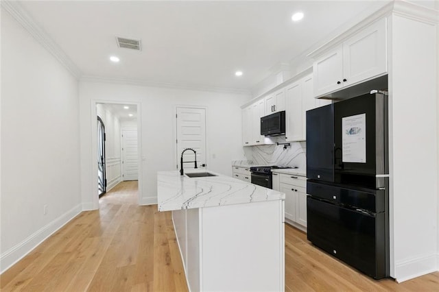 4544 Prairie St, Metairie, LA 70001 - kitchen with black appliances, white cabinetry, crown molding, an island with sink, and light stone counters