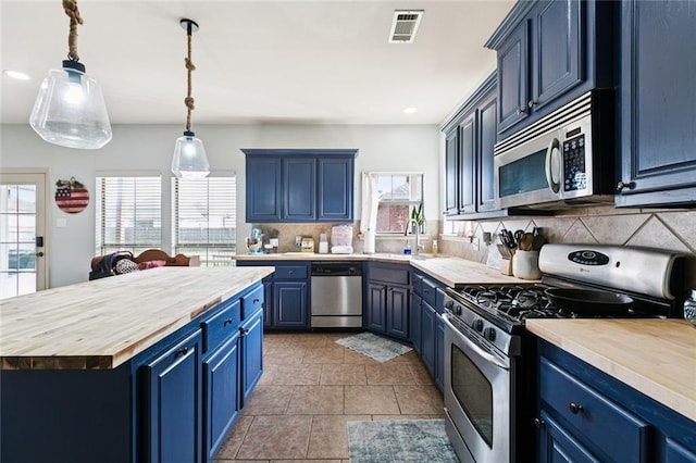 13795 Shady Hollow Dr, Denham Springs, LA 70726 - kitchen with appliances with stainless steel finishes, blue cabinets, butcher block countertops, decorative backsplash, and a kitchen island