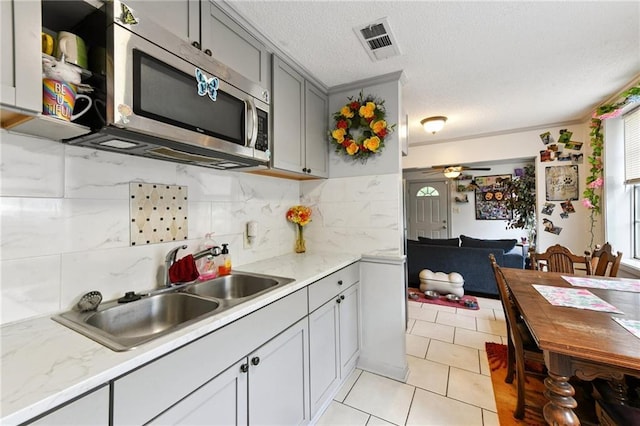 1500 Shirley Dr, New Orleans, LA 70114 - kitchen featuring stainless steel microwave, gray cabinetry, a ceiling fan, a textured ceiling, and decorative backsplash