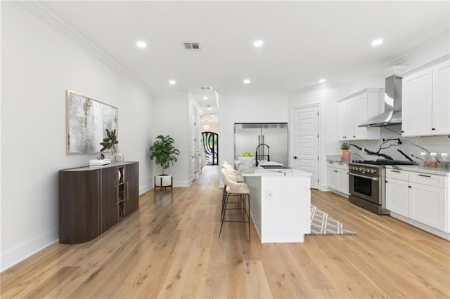 4542 Prairie St, Metairie, LA 70001 - kitchen with wall chimney exhaust hood, premium appliances, a kitchen breakfast bar, white cabinetry, and light countertops