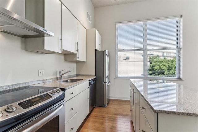 835 Julia St Unit 8, New Orleans, LA 70113 - kitchen with stainless steel appliances, wall chimney exhaust hood, light wood finished floors, white cabinets, and light stone countertops