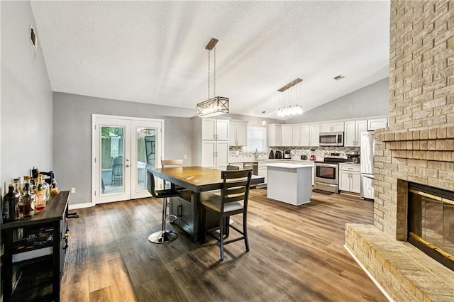 310 Oakley Ln, Destrehan, LA 70047 - dining area featuring vaulted ceiling, a textured ceiling, a brick fireplace, dark wood finished floors, and french doors