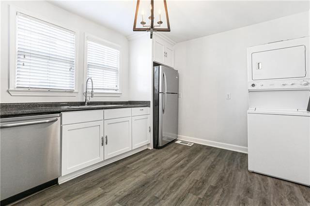 694244 Canal Blvd, New Orleans, LA 70115 - kitchen with appliances with stainless steel finishes, stacked washer / dryer, dark countertops, dark wood-type flooring, and white cabinets
