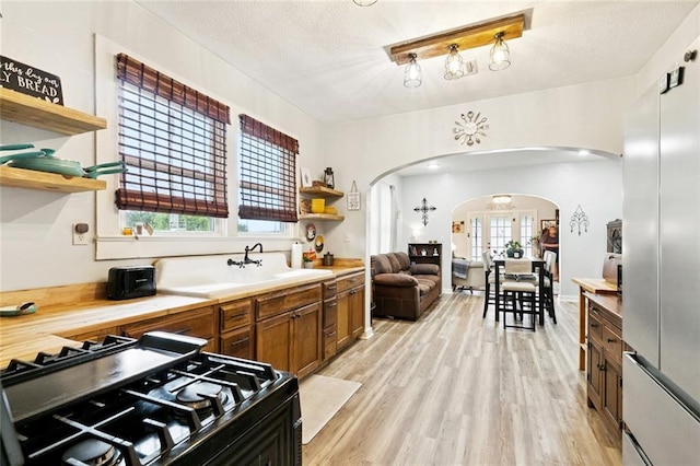 106 Rowley Blvd, La Place, LA 70068 - kitchen featuring arched walkways, open shelves, range with gas cooktop, light wood-style floors, and brown cabinetry