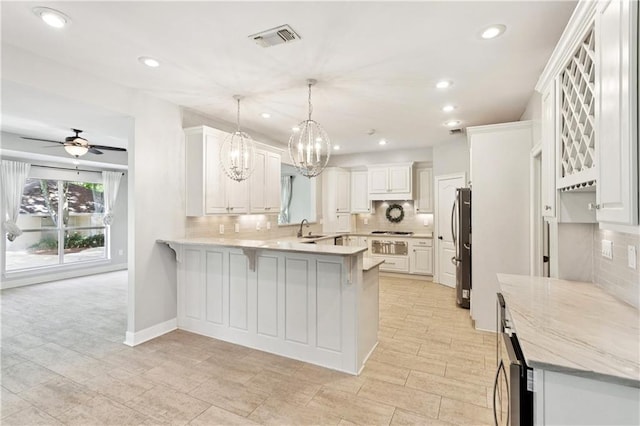 35 Elmwood Loop, Madisonville, LA 70447 - kitchen featuring a peninsula, decorative backsplash, a kitchen bar, freestanding refrigerator, and white cabinets