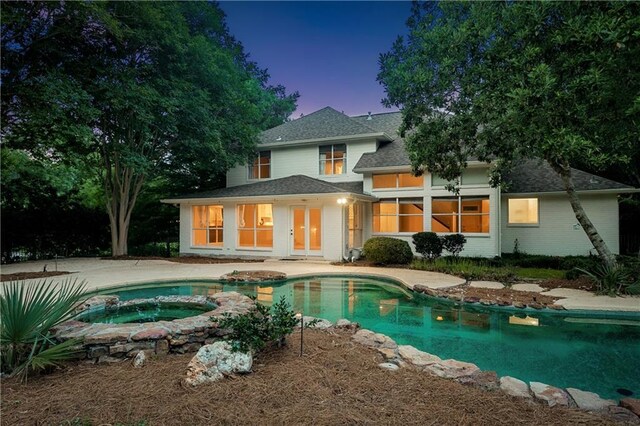 35 Elmwood Loop, Madisonville, LA 70447 - back of house at dusk featuring roof with shingles, a pool with connected hot tub, brick siding, and a patio