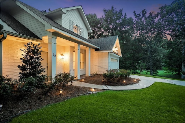 35 Elmwood Loop, Madisonville, LA 70447 - property exterior at dusk with brick siding, roof with shingles, a yard, a porch, and a garage