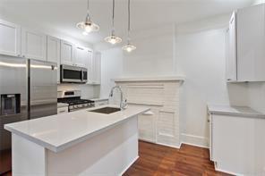 5227-29 Coliseum St, New Orleans, LA 70115 - kitchen featuring stainless steel appliances, light countertops, dark wood-style floors, a kitchen island with sink, and white cabinetry