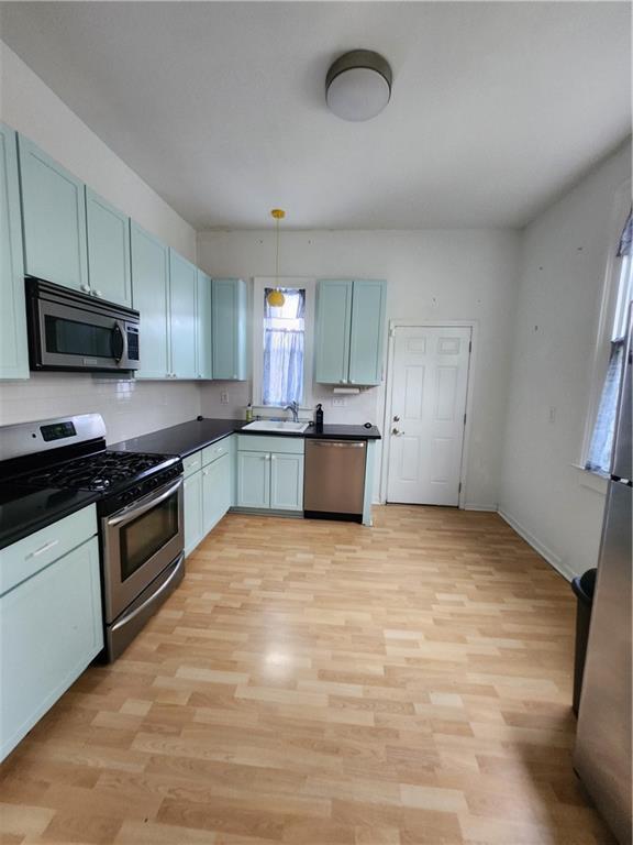 2715 Marengo St, New Orleans, LA 70115 - kitchen with stainless steel appliances, dark countertops, light wood-type flooring, and decorative light fixtures