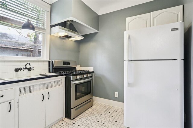 223840 Dante St, New Orleans, LA 70118 - kitchen featuring freestanding refrigerator, stainless steel gas stove, tile counters, range hood, and white cabinets