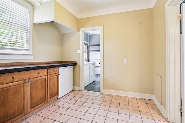223840 Dante St, New Orleans, LA 70118 - kitchen with white dishwasher, brown cabinets, dark countertops, light tile patterned floors, and washer / clothes dryer