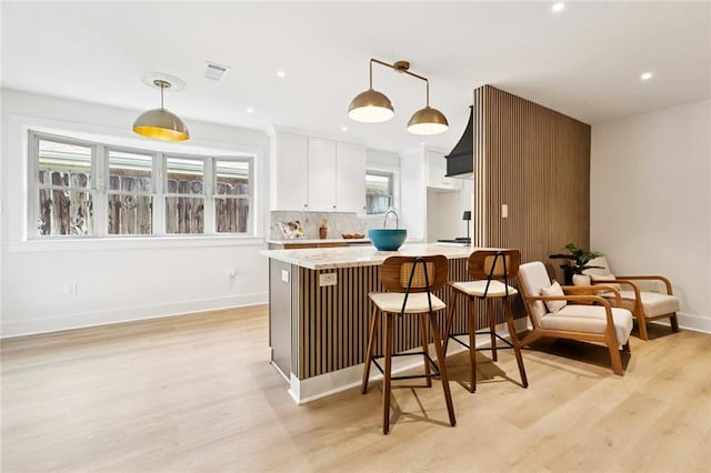 1528 N Cumberland St, Metairie, LA 70003 - kitchen featuring light wood-style floors, white cabinets, hanging light fixtures, a kitchen breakfast bar, and tasteful backsplash