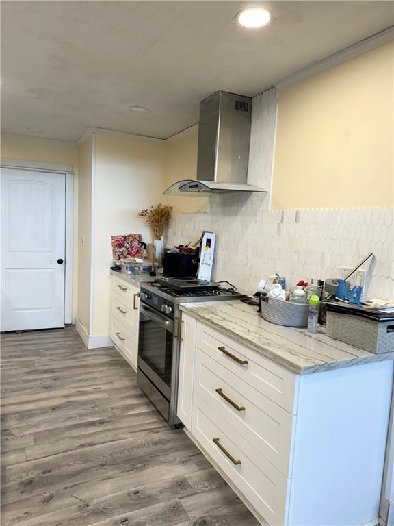 4925 Jasper St, Metairie, LA 70006 - kitchen featuring wall chimney exhaust hood, gas range, white cabinetry, wood finished floors, and light stone countertops