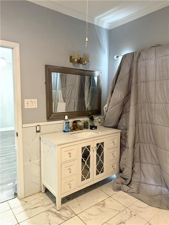4925 Jasper St, Metairie, LA 70006 - bathroom featuring marble look tiles, ornamental molding, vanity, and wainscoting