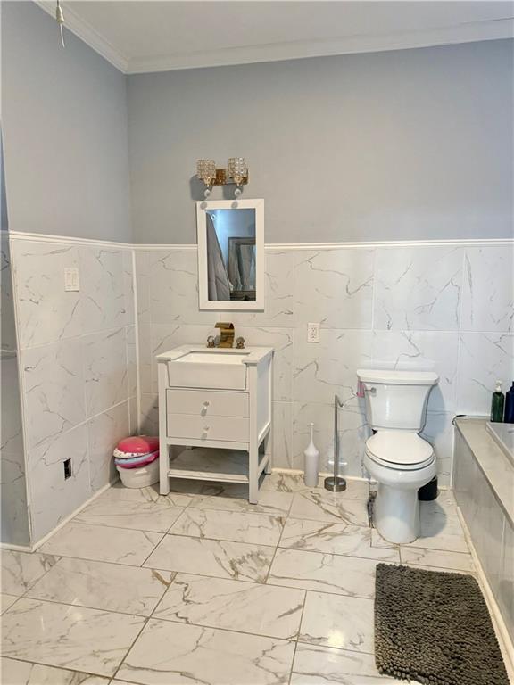 4925 Jasper St, Metairie, LA 70006 - full bathroom featuring vanity, tile walls, crown molding, marble finish floors, and wainscoting