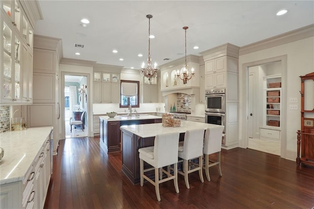 21 Royal Palm Dr, Kenner, LA 70065 - kitchen featuring an island with sink, a chandelier, dark wood-style floors, stainless steel double oven, and crown molding
