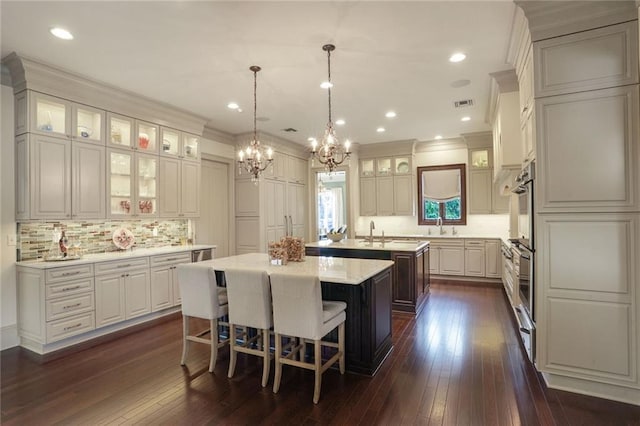 21 Royal Palm Dr, Kenner, LA 70065 - kitchen featuring a kitchen island with sink, a chandelier, tasteful backsplash, dark wood-style flooring, and crown molding
