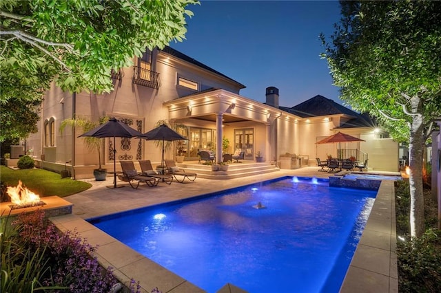 21 Royal Palm Dr, Kenner, LA 70065 - back of house at night with an outdoor fire pit, a patio, french doors, a pool with connected hot tub, and a chimney