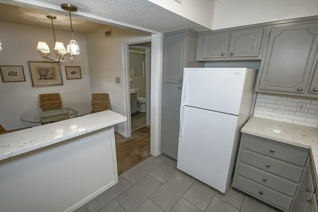 2708 Whitney Pl Unit 901, Metairie, LA 70002 - kitchen with freestanding refrigerator, gray cabinets, a chandelier, tasteful backsplash, and light stone counters