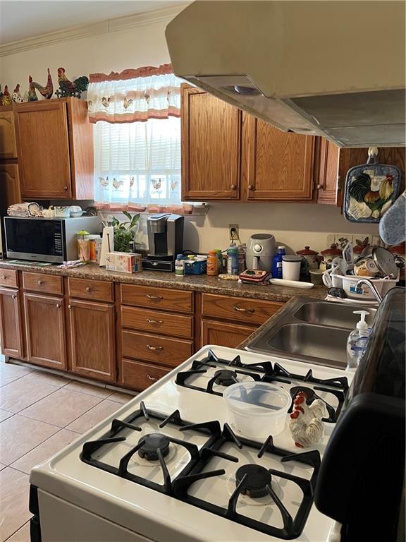 242830 A P Tureaud Ave, New Orleans, LA 70119 - kitchen with stainless steel microwave, brown cabinetry, exhaust hood, ornamental molding, and light tile patterned floors