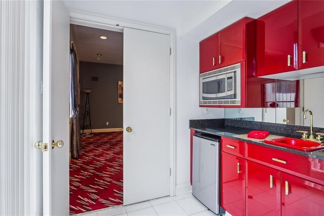 738 English Turn Ln, New Orleans, LA 70131 - kitchen with red cabinetry, stainless steel microwave, fridge, light colored carpet, and dark countertops
