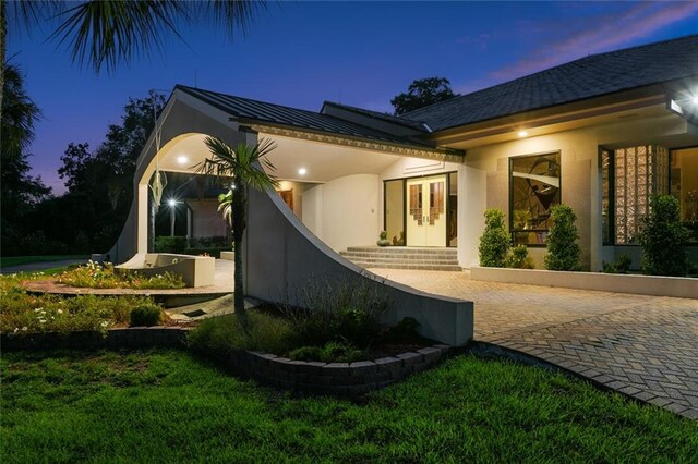 738 English Turn Ln, New Orleans, LA 70131 - exterior entry at dusk with french doors, stucco siding, a standing seam roof, and a metal roof