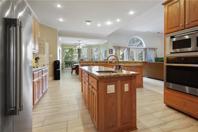 1071 Rue Chinon, Mandeville, LA 70471 - kitchen with stainless steel appliances, crown molding, an island with sink, brown cabinets, and a ceiling fan
