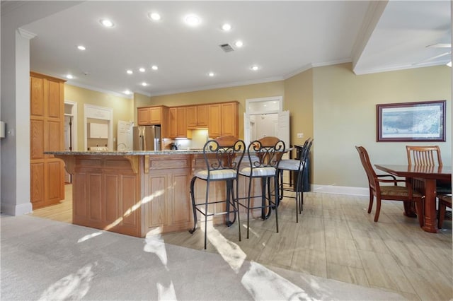 1071 Rue Chinon, Mandeville, LA 70471 - kitchen featuring freestanding refrigerator, recessed lighting, crown molding, a breakfast bar area, and light stone counters