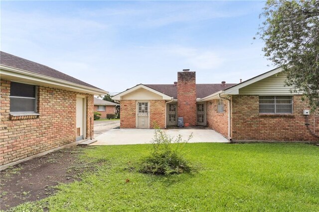 142 E Randall Ct, Gretna, LA 70053 - rear view of property featuring a patio, a chimney, a lawn, brick siding, and roof with shingles