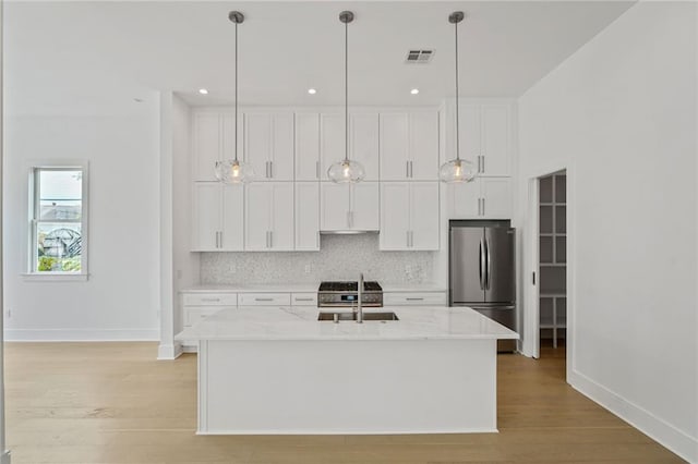 5310 Laurel St, New Orleans, LA 70115 - kitchen featuring freestanding refrigerator, backsplash, white cabinetry, light wood finished floors, and a center island with sink